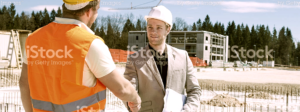 A construction worker shakes hands with a businessman on a construction site.
