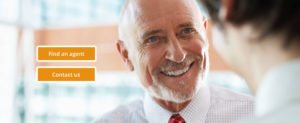 An older businessman wearing a collared shirt and red tie warmly smiles to another man facing him. Two options button on the image read "Find an agent" and "contact us".